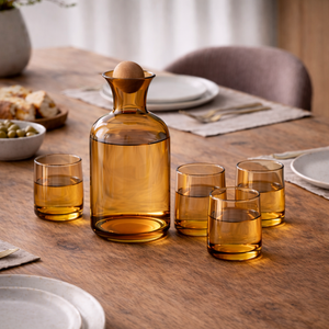 Amber glass water carafe with a round stopper and four tumblers on a dining table