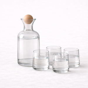 Clear glass water carafe and four matching tumblers on a light background