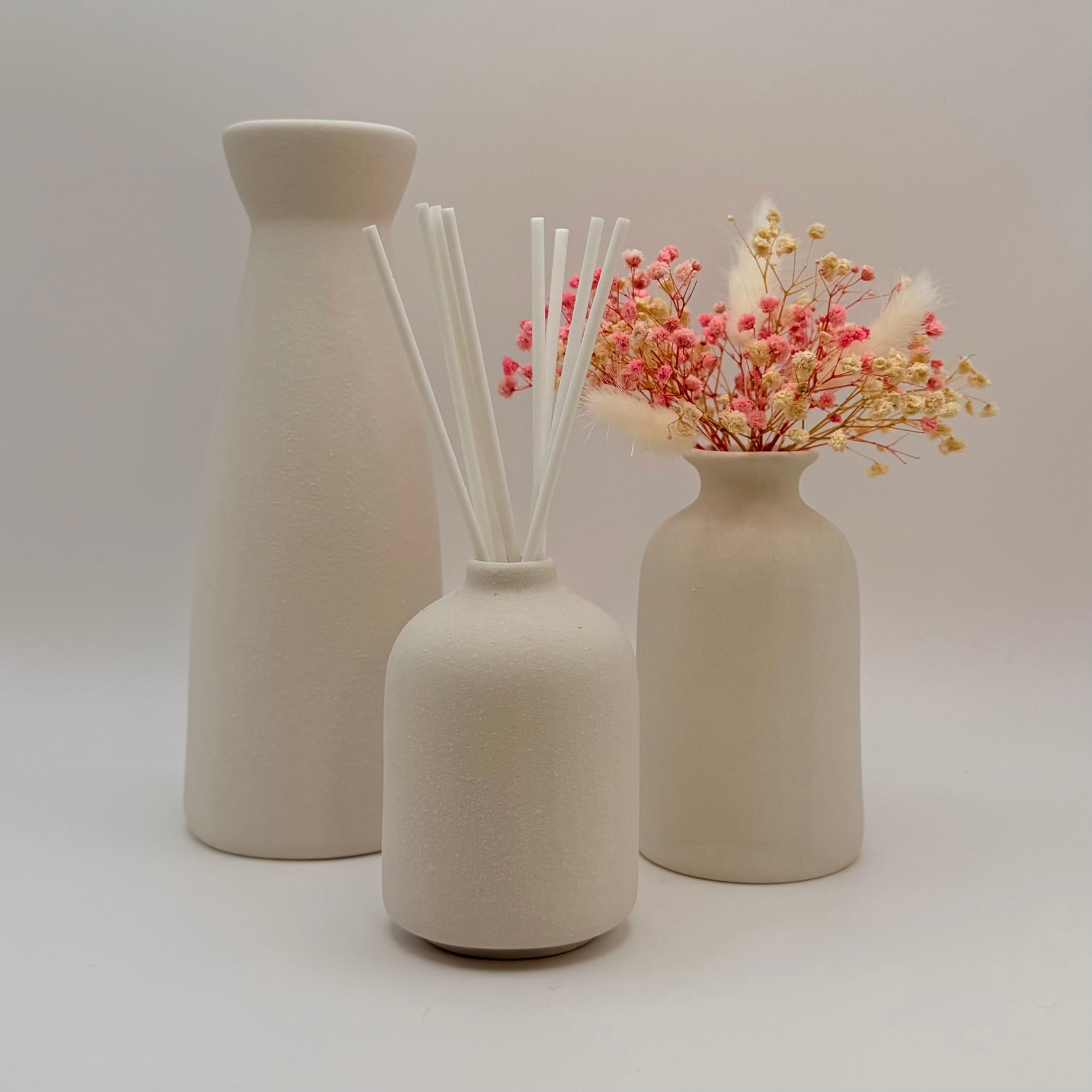 Three cream ceramic vases with dried flowers and white diffuser reeds
