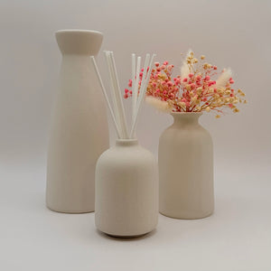 Three cream ceramic vases with dried flowers and white diffuser reeds