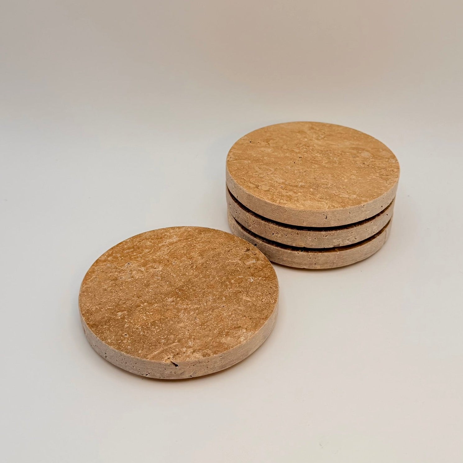 Four round travertine coasters with dark edges on a light background