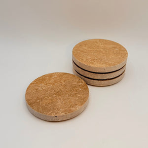 Four round travertine coasters with dark edges on a light background
