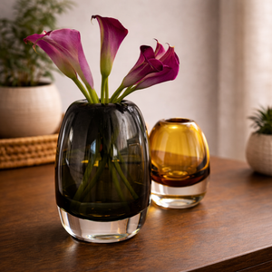 Large gray glass bud vase holding purple flowers beside a small amber vase