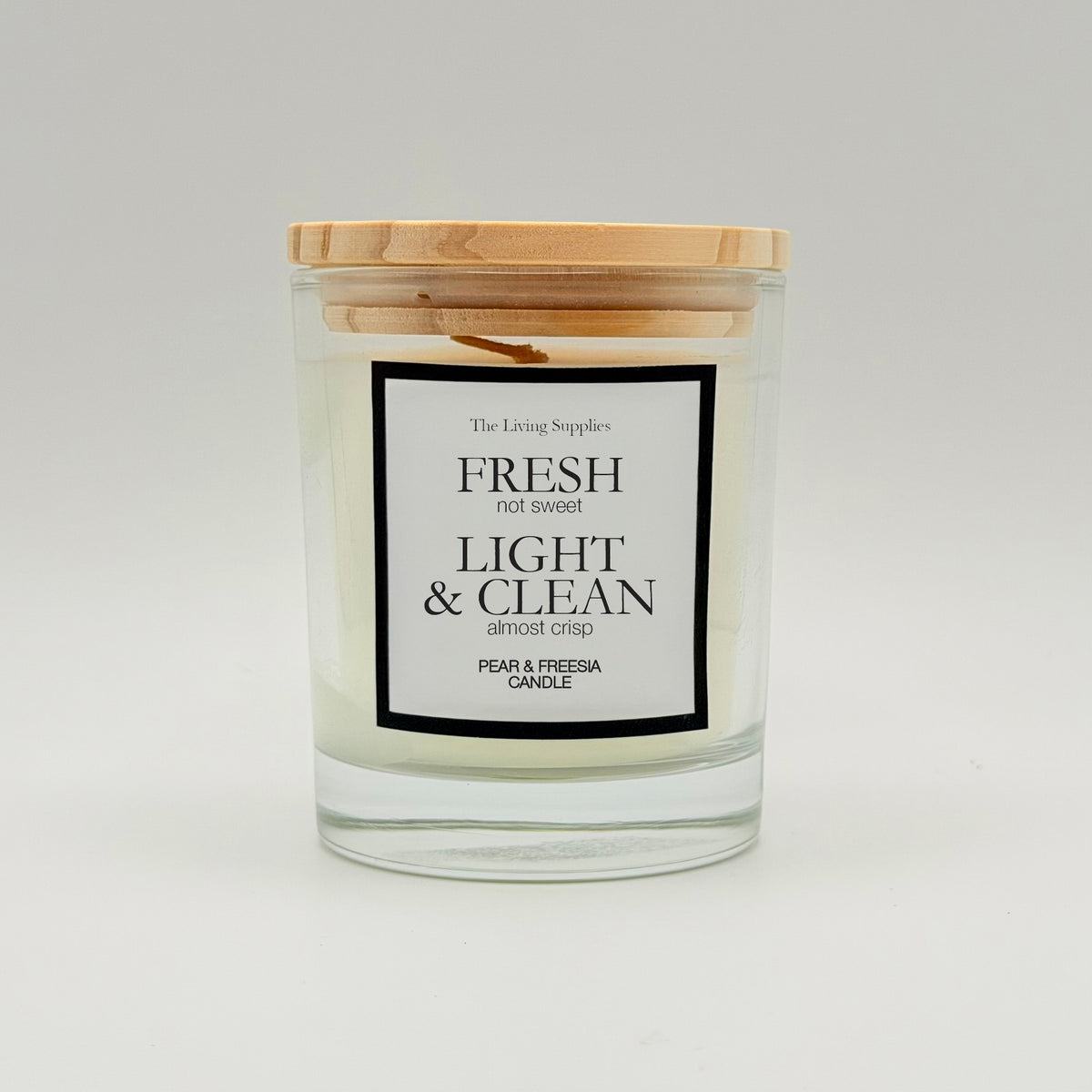 Pear and freesia candle in a clear glass jar with a wooden lid and black-bordered label