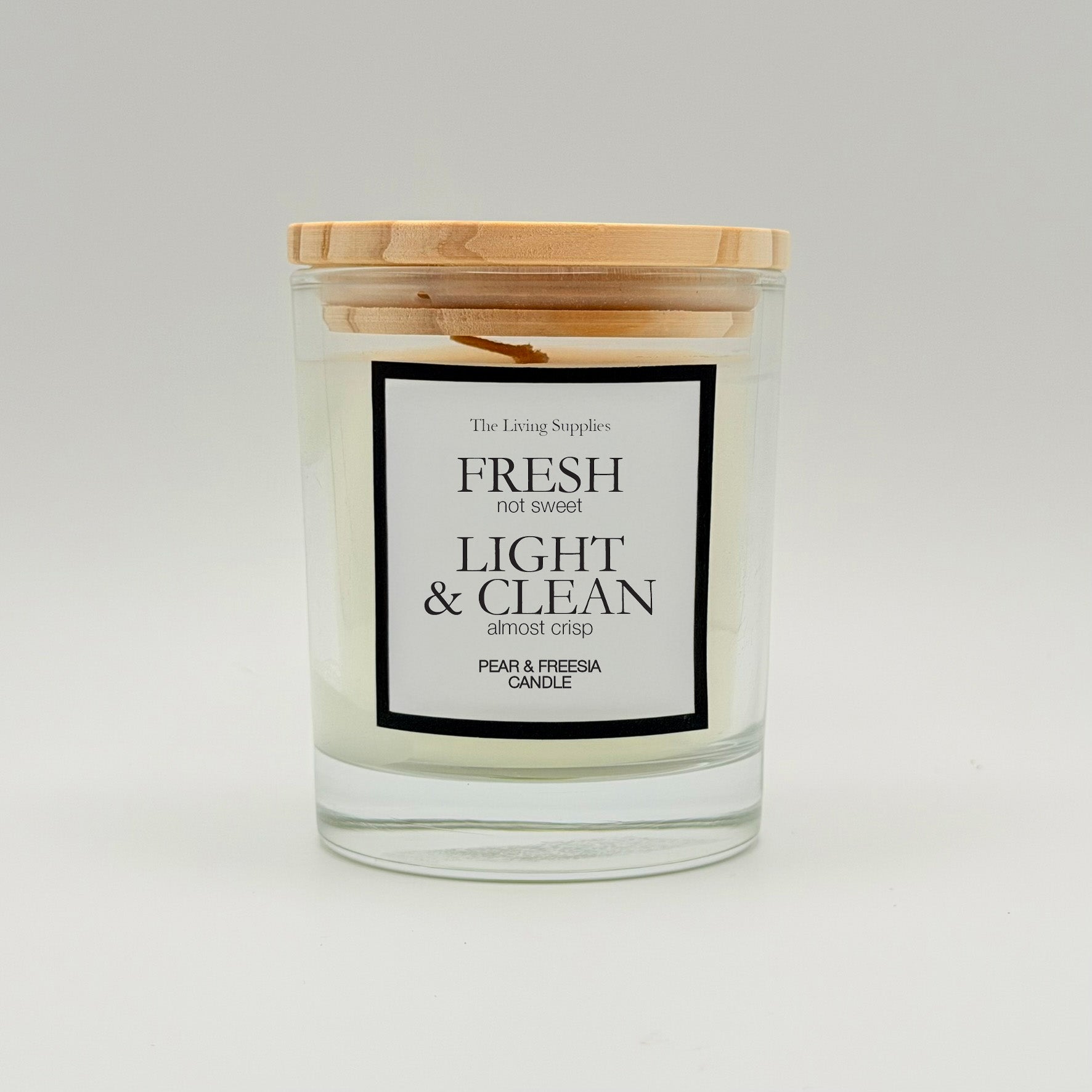Pear and freesia candle in a clear glass jar with a wooden lid and black-bordered label