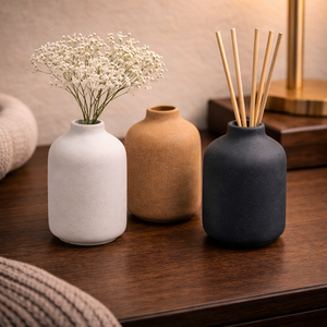Three sand-glazed ceramic bud vases on a wooden table, with dried flowers and diffuser reeds