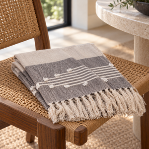 Gray and neutral striped handloomed cotton slub throw with tassels on a woven chair