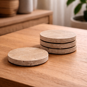 Four round travertine coasters, three stacked and one on a wooden table